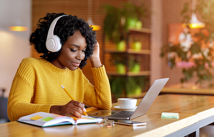Una giovane donna che studia alla scrivania con un computer portatile, le cuffie e un quaderno.